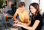 Two women sit at a countertop looking at a laptop together