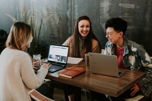 Three people sitting around a table with computers and laughing