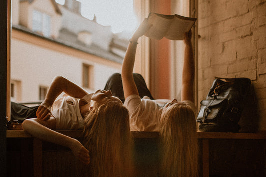 Two girls lie on their backs in front of a sunny window