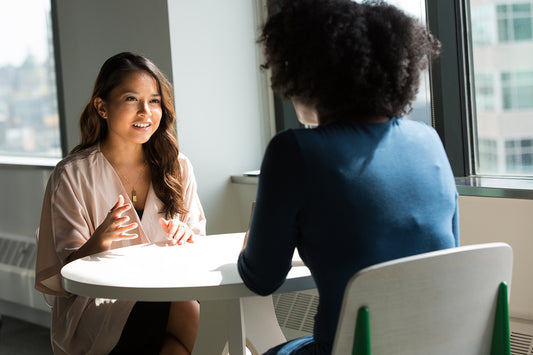 Two women sit across a table talking to each other