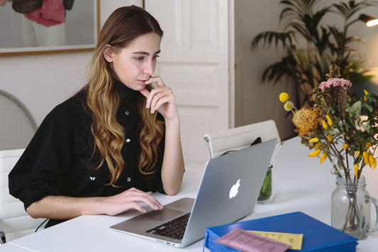A woman sits at a laptop on a white desk with flowers