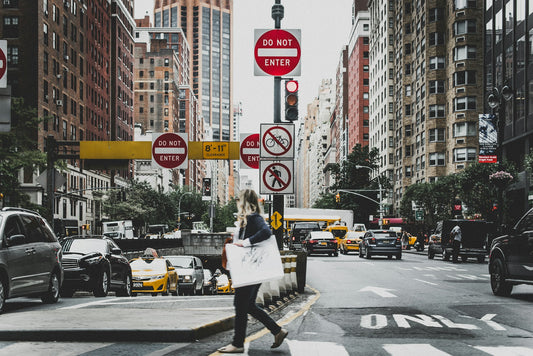 a busy new york city street scene with a women crossing the stress with a big bag