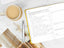 A yellow planner open on a marble tabletop next to a cup of tea and a magazine