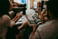 Two people sit together talking while looking at a phone and a magazine