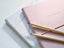 A pink notebook on top of a white notebook, with two colored pencils on top