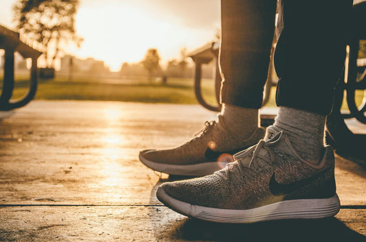 Two feet in grey sneakers on a sidewalk in front of a setting sun