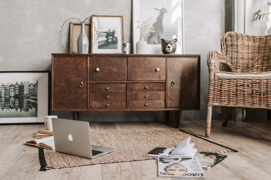 A living room with a credenza, a wicker chair, and a laptop sitting on the floor