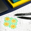 Coloring book with geometric designs, markers, and a laptop on a blue surface