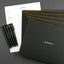 Black notebooks with gold accents and pens on a gray background