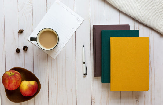 A fall scene with apples, tea, and planners on a rustic wooden table.