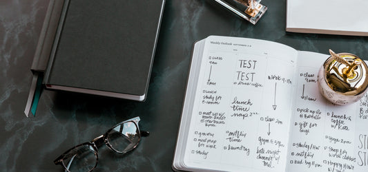 A time blocking planner filled out for a busy school week on a desk with a notebook and glasses.