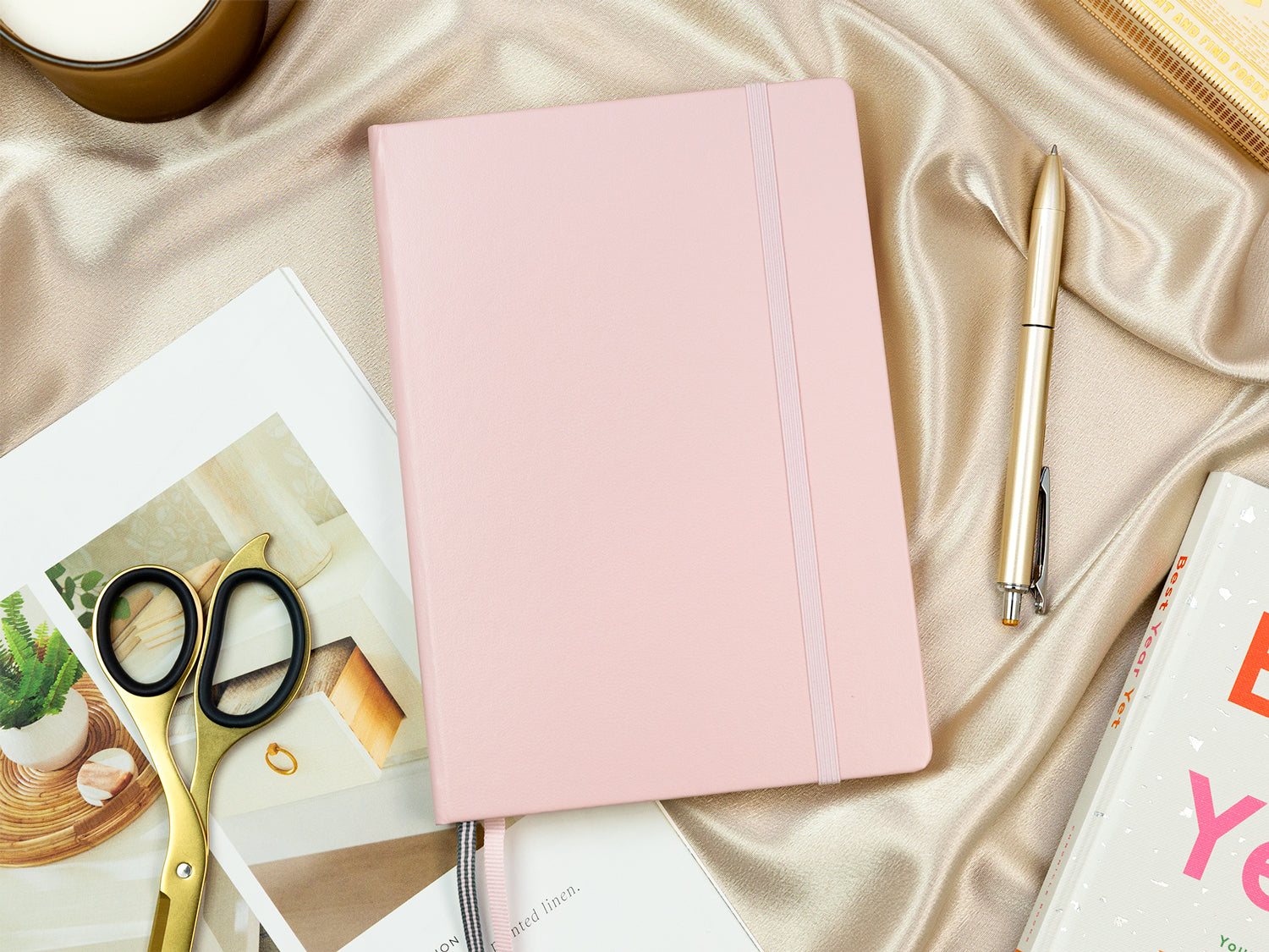 A pink planner on top of a gold sheet next to gold desk accessories