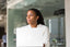 A woman sits at a laptop looking off into the distance