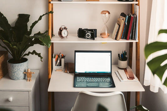 A black computer sits on an organized white desk with green plants