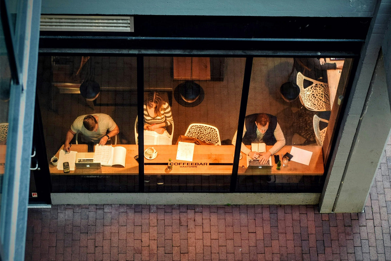 A window showing three people sitting at a bar inside a building at night