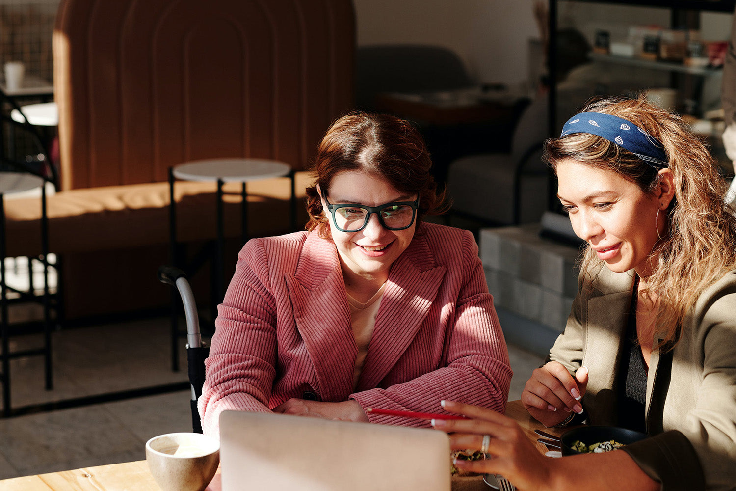 Two women sit at a table looking at a laptop together