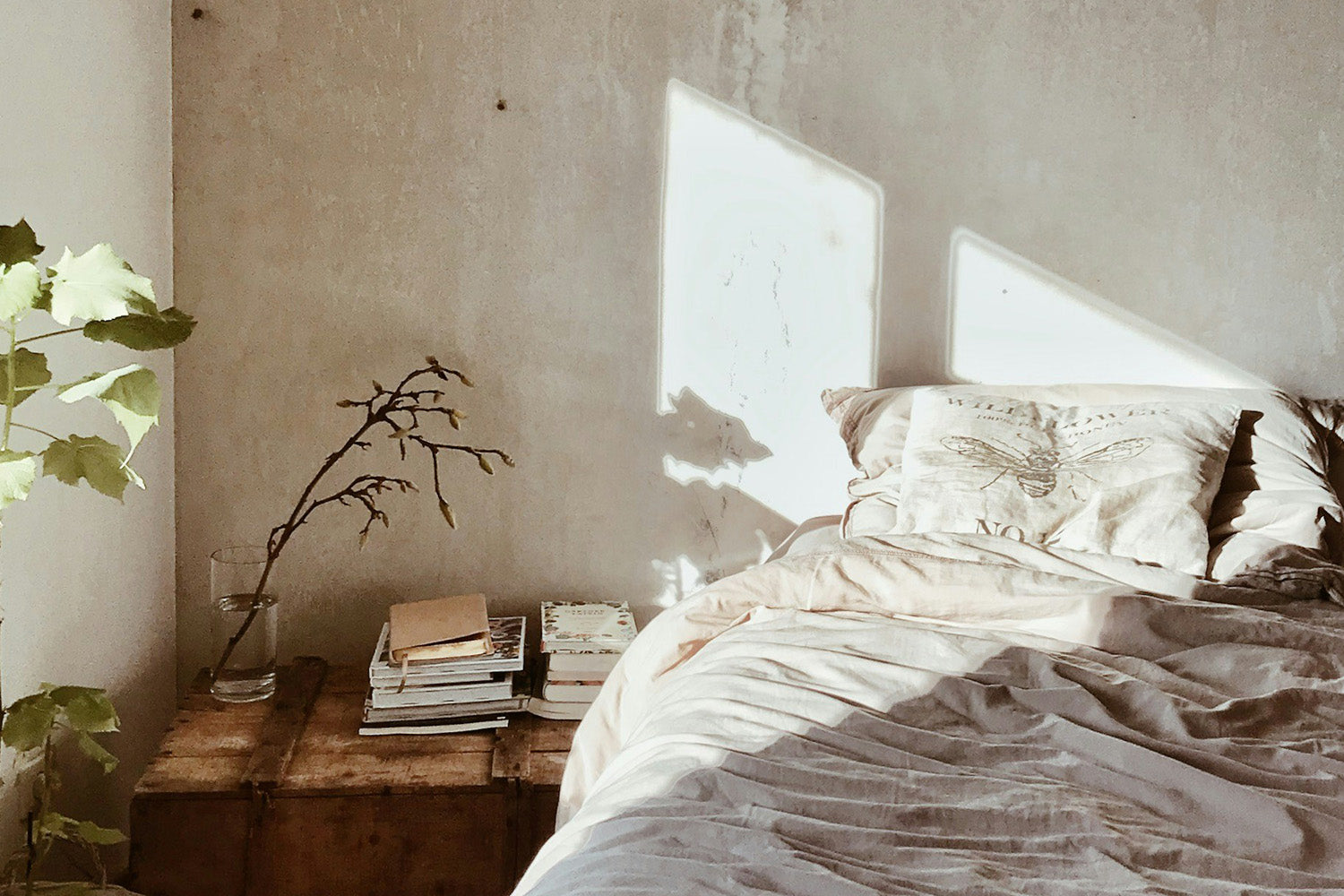 A bed with white bedding next to a stack of books on the floor