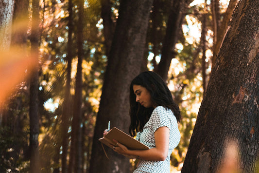 A woman stands in a forest and writes in a notebook