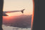 View out of an airplane window, showing an airplane wing and a sunrise over mountains
