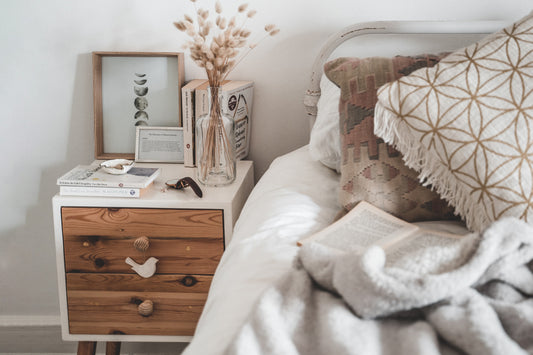 A wood and white nightstand next to a bed with tan pillows and white bedding.