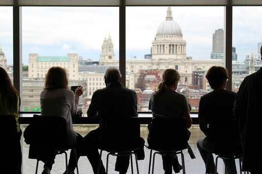 A row of people sit at a table in front of a large window