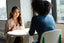 Two women sit across a table talking to each other
