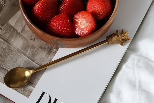 A gold spoon next to a bowl of strawberries