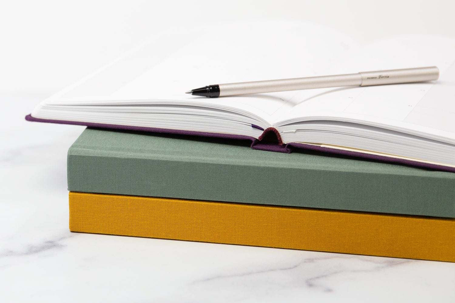 A stack of three planners, with the top one open and a pen sitting on top.