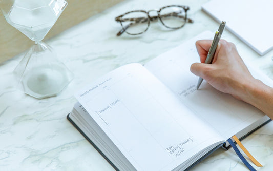 An Ink+Volt Planner is on a desk and someone is writing in it