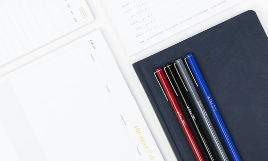 Notepads and an array of colorful pens on a white tabletop.