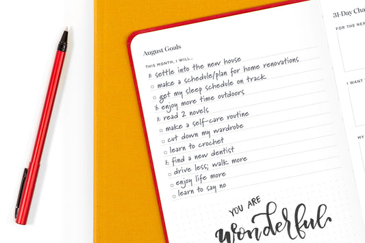 A planner with a list of goals, including health and wellness goals, next to a red pen on a white table.