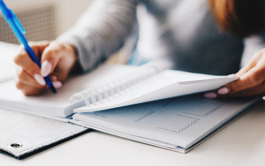 A woman writes in a planner with a blue pen.