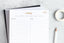 An organizing pad, a planner, and a pencil on a marble tabletop.