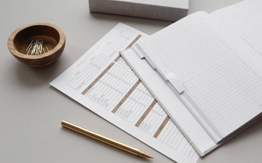 An array of planning tools and worksheets sit on a desk next to a pencil and a wooden cup with paper clips in it.