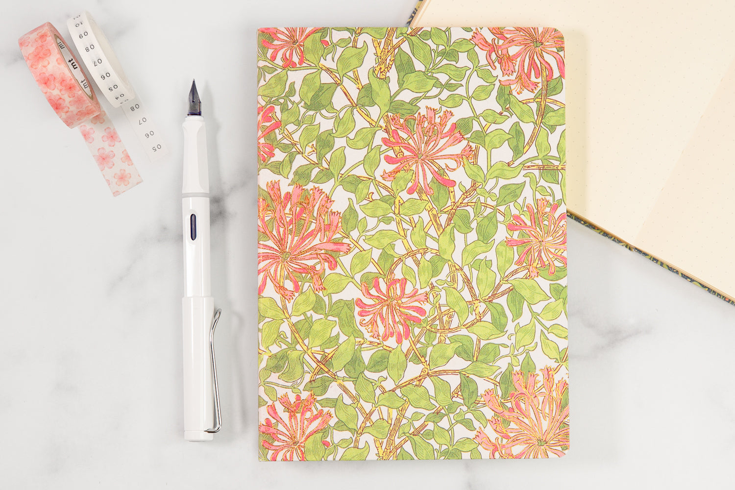 A floral bullet journal notebook on a white table next to a white pen.