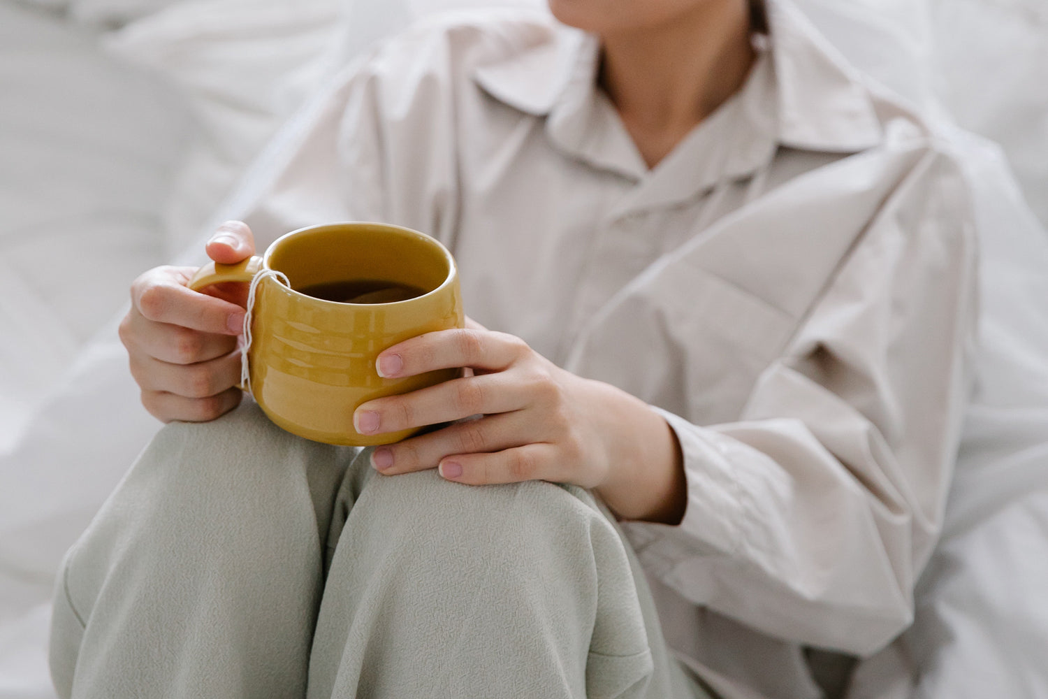 Girl sitting on a bed with a yellow coffee mug