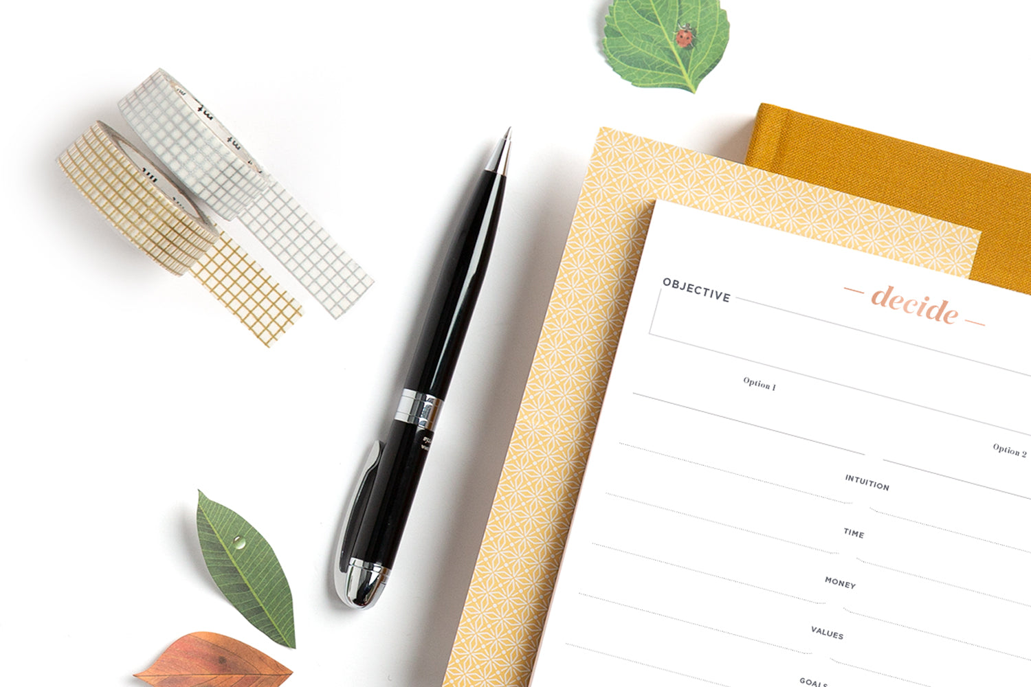 An array of cute office supplies for fall, including a pen, a decision notepad, grey and silver washi tape, and a goldenrod ink+volt planner.
