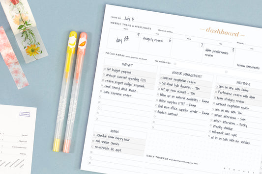 A dashboard project management pad filled in with to-do's on a blue desk next to two pens and washi tape.