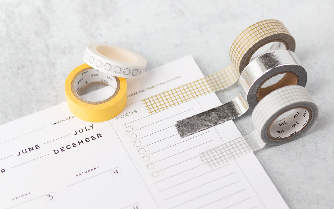 Four rolls of colorful decorative tape and washi tape decorate a weekly desk pad calendar.