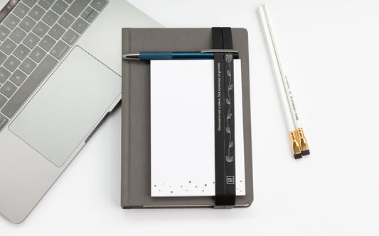 A stack of office desk accessories: a planner with book bands, a notepad, a pen, and two pencils.