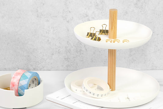 A white two-tiered desk organizer with gold accessories on it, on a white desk.