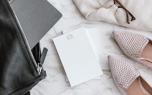 Ink+Volt Faceted Foil notepads sit on a marble surface surrounded by a sweater, eyeglasses, a woman's flats, a purse, and an Ink+Volt planner