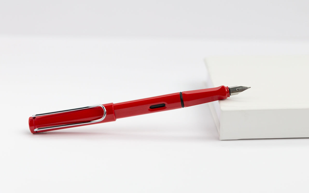 A red fountain pen is propped up on a white planner on top of a while table.