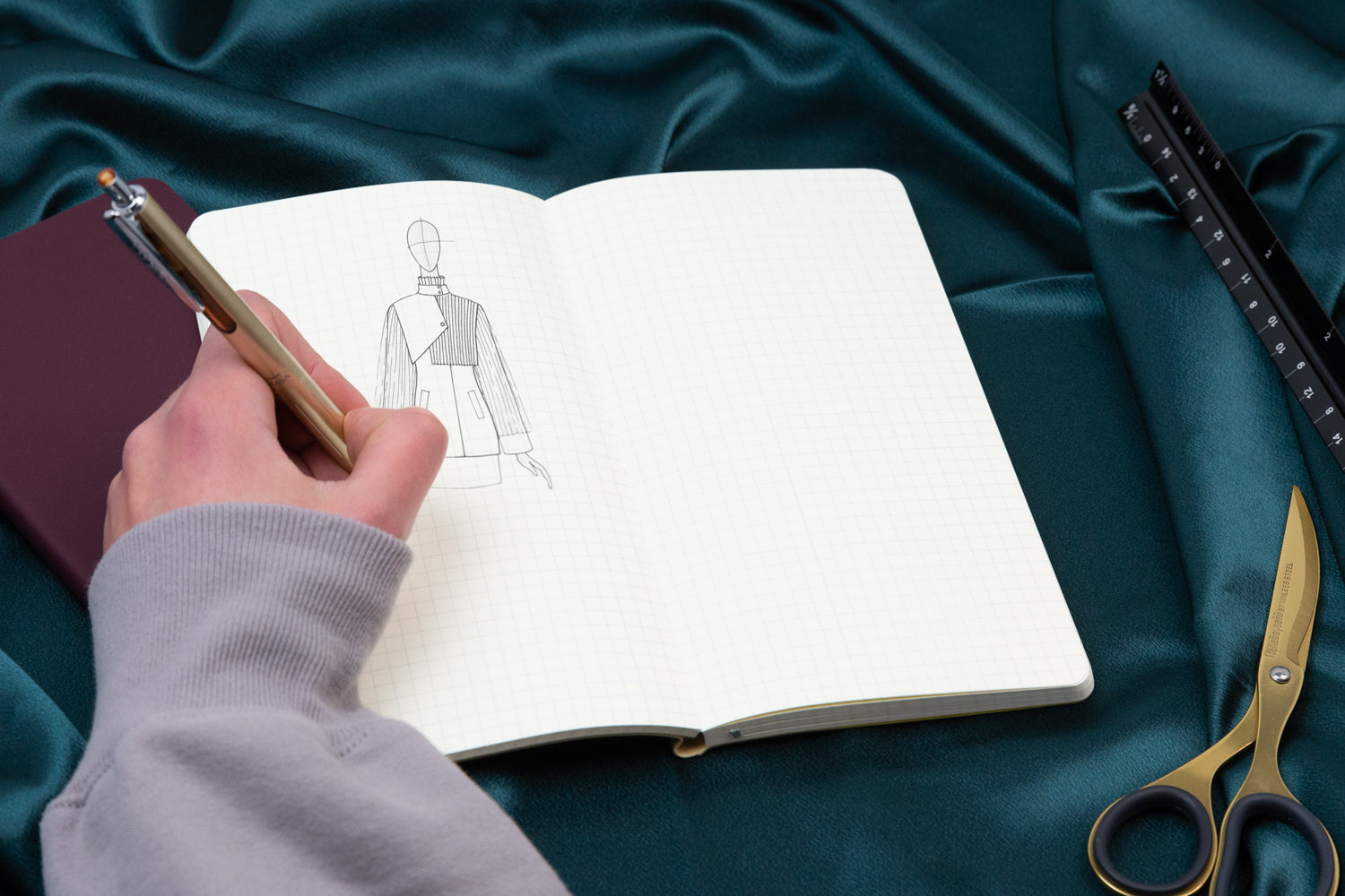 person drawing a fashion figure in a gridded notebook