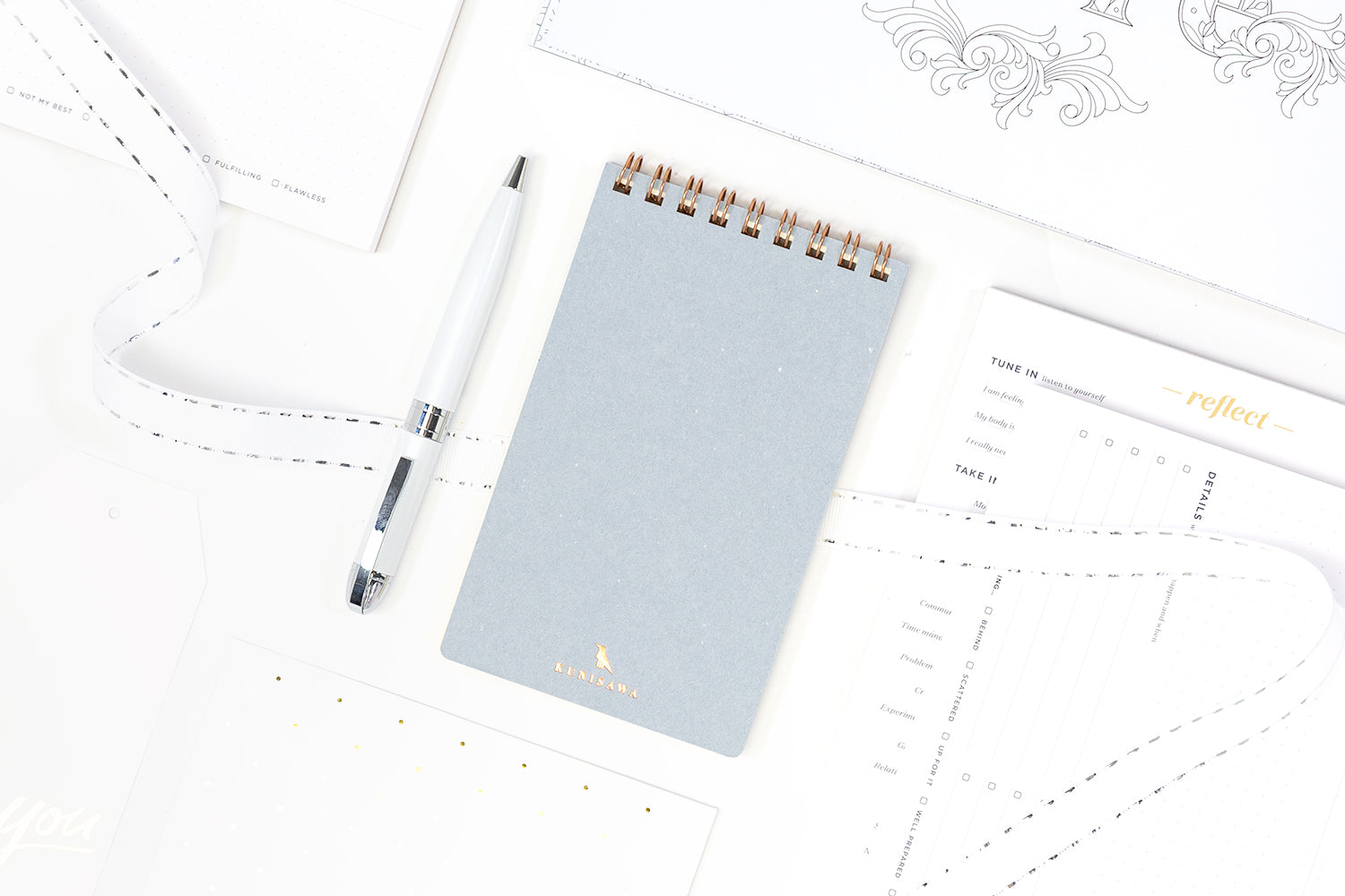 A collection of secret santa gift ideas including a pale blue notepad, a pen, and productivity notepads.