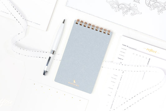 A collection of secret santa gift ideas including a pale blue notepad, a pen, and productivity notepads.