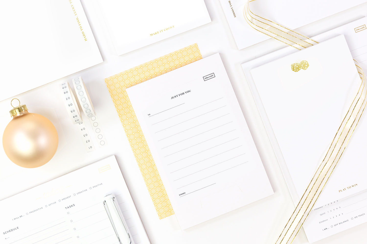 A bright, white assortment of small gifts for coworkers: white and gold notepads, gold ribbons, and a gold holiday ornament.