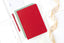 A red planner on top of an array of notepads, next to a red pen and a gold ribbon.
