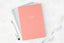 A stack of pink, blue, and lavender gratitude journals on a white table, with a white pen.