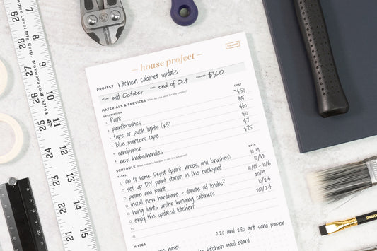 A house project notepad on a table, surrounded by tools such as a ruler, wrench, and pencils.